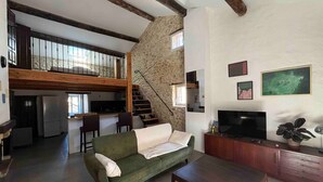 Un ampio soggiorno con un divano verde, un tavolino di legno, una TV e un muro in pietra.