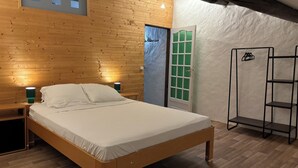 Una camera da letto con un letto di legno, un comodino, una lampada illuminata di verde, una porta bianca con un oblò verde e una mensola in metallo nero.