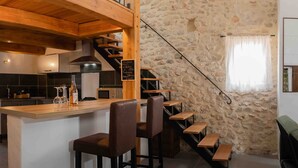 Una cucina con isola centrale, sgabelli da bar, parete in pietra e una scala.