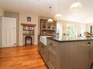 A kitchen with wooden cabinets, a central island, pendant lights, and a bookshelf. - Hathaway Lane in Warwickshire. (Stratford-upon-Avon)