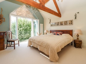 A bedroom with a large bed, a chair, a lamp, and a window with a view of greenery. - Hathaway Lane in Warwickshire. (Stratford-upon-Avon)