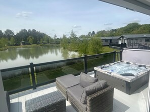 Un balcón con un jacuzzi, mobiliario de mimbre y vistas a un lago y edificios.