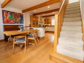 A spacious kitchen with wooden cabinets, a dining area with a wooden table and chairs, and a staircase leading to an upper level. - Rowan Tree Cottage, Skipton (Skipton)