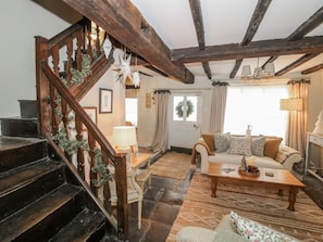 Un escalier en bois avec une rampe, un salon avec un canapé et une table basse, et une porte décorée d’une guirlande.