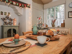 Une cuisine chaleureuse avec une table en bois, un sapin de Noël et une fenêtre donnant sur un paysage verdoyant.