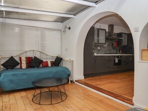 A compact living space with a sofa, a round table, a kitchen area, and an arched doorway. - Teign Place, Teignmouth (Teignmouth)