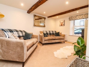 A cozy living room with two sofas, a white fur rug, a wooden ceiling beam, a mirror, and a window with a car outside. - Cobble Cottage, Gisburn (Clitheroe)