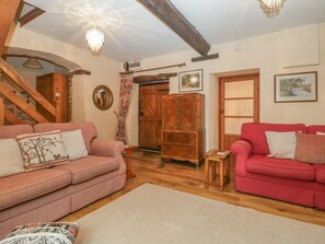 A living room with two sofas, a wooden cabinet, a staircase, and a chandelier.