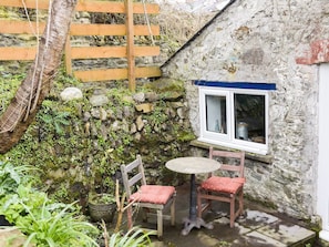 A stone cottage with a small window, a wooden fence, and a table with chairs.