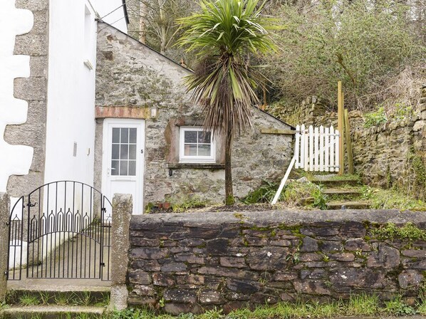 A stone house with a white door, a small window, and a white picket fence.