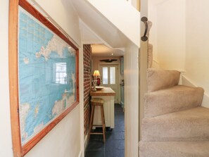 A hallway with a large world map, a kitchen area with a stool, and a carpeted staircase.
