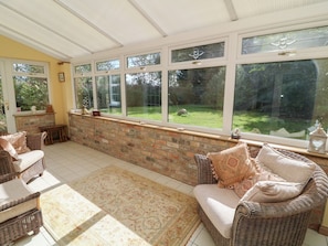 A sunlit room with wicker furniture, a brick wall, and large windows overlooking a garden.