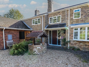 A two-story brick house with a gravel driveway, a wooden bench, and a small garden area.