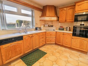 A kitchen with wooden cabinets, a dishwasher, a sink, a window with a view, and a hexagonal floor pattern. - Ritas, nr Kilkeel, County Down (Newry)
