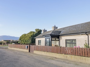 A single-story house with a sloped roof, a wooden fence, and a gravel driveway. - Ritas, nr Kilkeel, County Down (Newry)