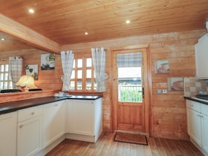A wooden cabin-style kitchen with a wooden door, white cabinets, a black countertop, and a window with curtains. - Pine, Swanage, Dorset AONB, TV (Swanage)