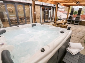 A hot tub in an outdoor patio area with a wooden table and chairs, stone walls, and a brick oven in the background. - Poacher's Arms, Hope (Hope Valley)