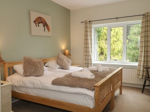 A bedroom with a wooden bed, a nightstand, a lamp, a window with curtains, and a painting on the wall. - Poacher's Arms, Hope (Hope Valley)