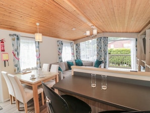 Um quarto acolhedor com teto de madeira, uma mesa de jantar com cadeiras, um sofá com almofadas e uma janela com cortinas.