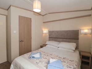 A bedroom with a bed, two bedside lamps, a wooden door, and a nightstand. - Beech: Charming Retreat in Swanage (United kingdom)