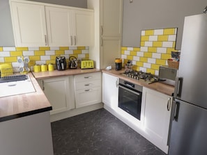 A kitchen with white cabinets, a black countertop, a stove, an oven, and a refrigerator. - The Yellow House in Withernsea (Withernsea)