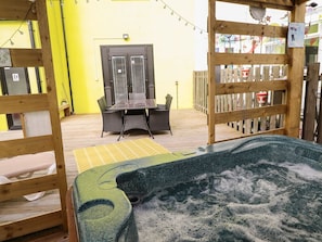 A wooden deck with a hot tub, a table with chairs, and a fenced area with a gate. - The Yellow House in Withernsea (Withernsea)