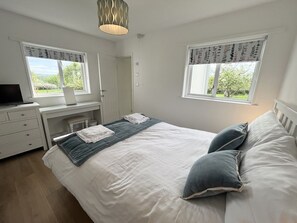 A bedroom with a bed, two windows, a desk, a chair, a lamp, and a television. - War Horse Valley Orchard View, Hatherleigh (Winkleigh)