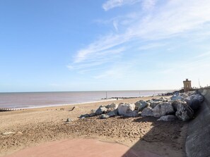 Ein Strand mit einer Steinmauer, einem Turm und wolkenlosem Himmel.