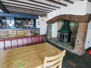 A bar area with a stone fireplace, wooden seating, and a bar counter with various bottles. - Manor House Gold 2 Bedroom (20C), Aspatria (Maryport)