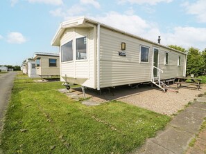 A single-story mobile home with a front porch, a small attached structure, and a gravel driveway. - Manor House Gold 2 Bedroom (20C), Aspatria (Maryport)