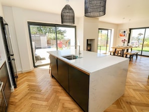 Una cocina moderna con una isla grande, armarios oscuros y un suelo de madera en espiga.