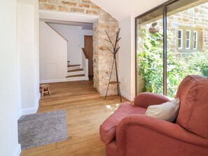 Ein Wohnzimmer mit einem roten Sofa, Holzboden, Steinwand und Blick auf Grünfläche.