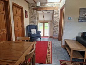 A room with a wooden dining table, a blue armchair, a red rug, and a stone wall. - Kingfisher Cottage, Llanboidy (Whitland)