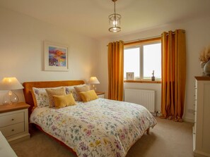 A bedroom with a bed, two bedside tables, a window with curtains, a radiator, and a painting on the wall. - Taigh Eva, Lochmaddy, North Uist (Isle of North Uist)