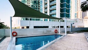 A swimming pool with a tiled deck, surrounded by modern buildings. - Live the Vibe Upgraded 2BR JBR Coastal Living (Dubai)