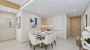 A modern dining area with a round table, white chairs, and a kitchen in the background. - Live the Vibe Upgraded 2BR JBR Coastal Living (Dubai)