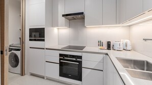 A modern kitchen with built-in appliances, a stainless steel sink, and a compact layout. - Live the Vibe Upgraded 2BR JBR Coastal Living (Dubai)