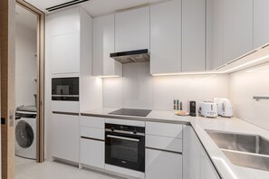 A modern kitchen with built-in appliances, a stainless steel sink, and a compact layout. - Live the Vibe Upgraded 2BR JBR Coastal Living (Dubai)