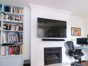 A living room with a fireplace, a bookshelf, a mounted TV, and a desk with a computer. - Fairhazel Apartment, Hastings (Hastings)