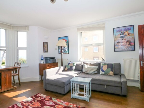A living room with a grey sofa, a small white table, a patterned rug, a lamp, and a poster on the wall. - Fairhazel Apartment, Hastings (Hastings)