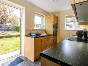 A kitchen with wooden cabinets, a black countertop, and a window. - Sweetacres Retreat in Hemsby (Great Yarmouth)