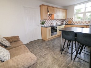 A compact kitchen with wooden cabinets, a black countertop, and a dining area with bar stools. - Woodside Guest House, Castlerock (Coleraine)