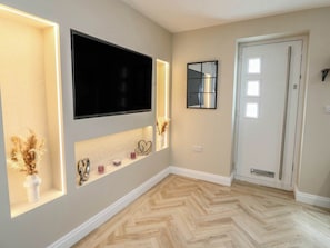 A room with a large flat-screen TV mounted on the wall, a mirror, and a door with a handle. - Hen Siop, Niwbwrch (newborough) (Llanfairpwllgwyngyll)