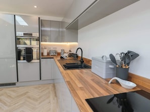 A modern kitchen with a built-in oven, a toaster, a kettle, and a sink. - Hen Siop, Niwbwrch (newborough) (Llanfairpwllgwyngyll)