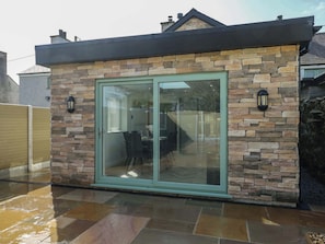 A modern house with a stone exterior, a sliding glass door, and a patio area. - Hen Siop, Niwbwrch (newborough) (Llanfairpwllgwyngyll)