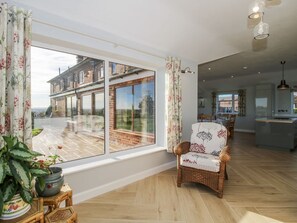 A spacious room with a large window, wicker furniture, and a view of a brick building. - Garden Cottage, Cockshutt (Ellesmere)