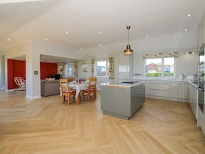 A modern kitchen with a central island, dining area with chairs, and a view of the outdoors. - Garden Cottage, Cockshutt (Ellesmere)