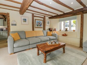 Ein Wohnzimmer mit grauem Sofa, Holzbalken, einem Couchtisch und gerahmten Kunstwerken an den Wänden.