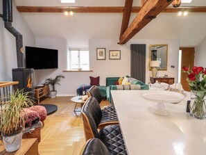 A cozy living room with a fireplace, a sofa, a dining table, and a TV. - The Old Cartshed | Yr Hen Gwt Cart, Llangernyw (Abergele)