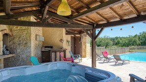 Un bain à remous sous une pergola en bois, avec une piscine et des chaises longues en arrière-plan.